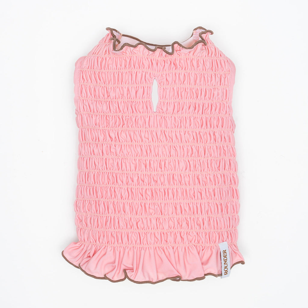 Pink smocked dress with ruffled trim on a white background